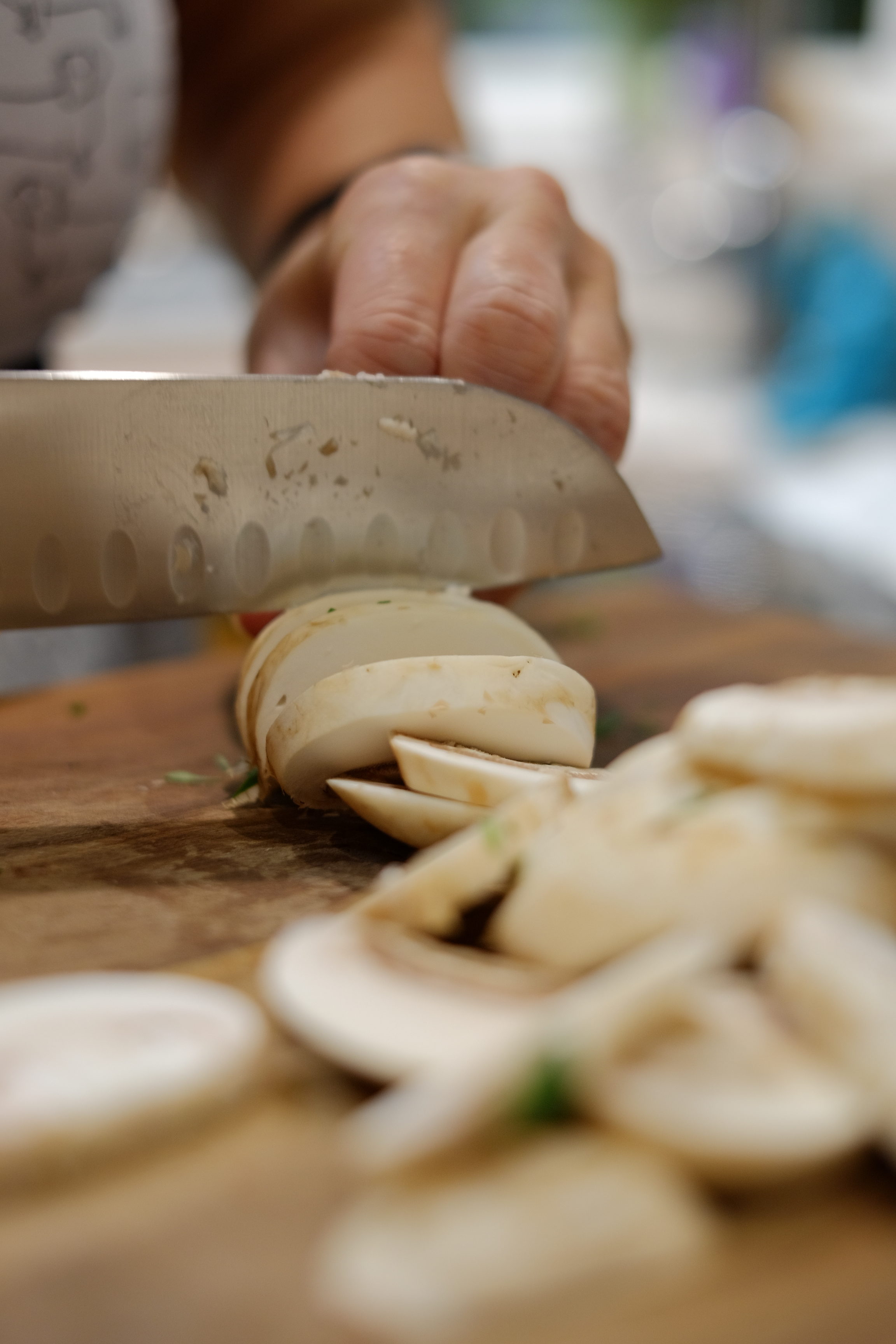 Close up shot of knife cutting through mushrooms on walnut chopping board.