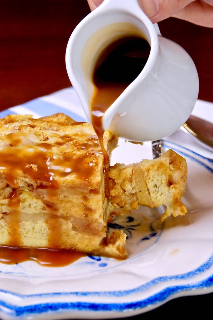 Apple Cider Caramel Sauce being poured over a serving of Apple Cinnamon Strata on a white and blue plate.