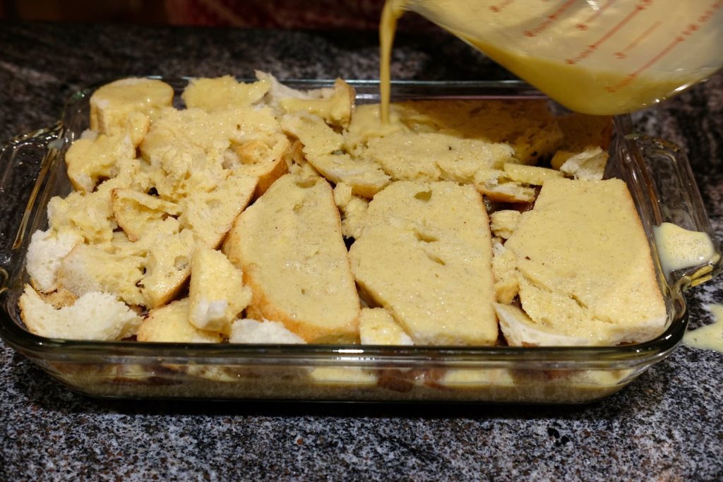 Apple Cinnamon Strata pouring custard over bread in baking dish