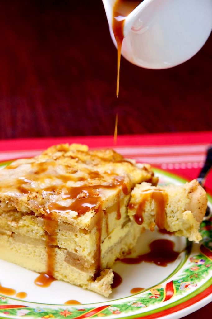 Apple Cinnamon Strata being drizzled with Apple Cider Caramel Sauce on Christmast plate set on red linen.