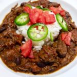Brazilian Beef Stew Feijoada served with white rice and garnishes with chopped tomato and jalapeno in White Bowl