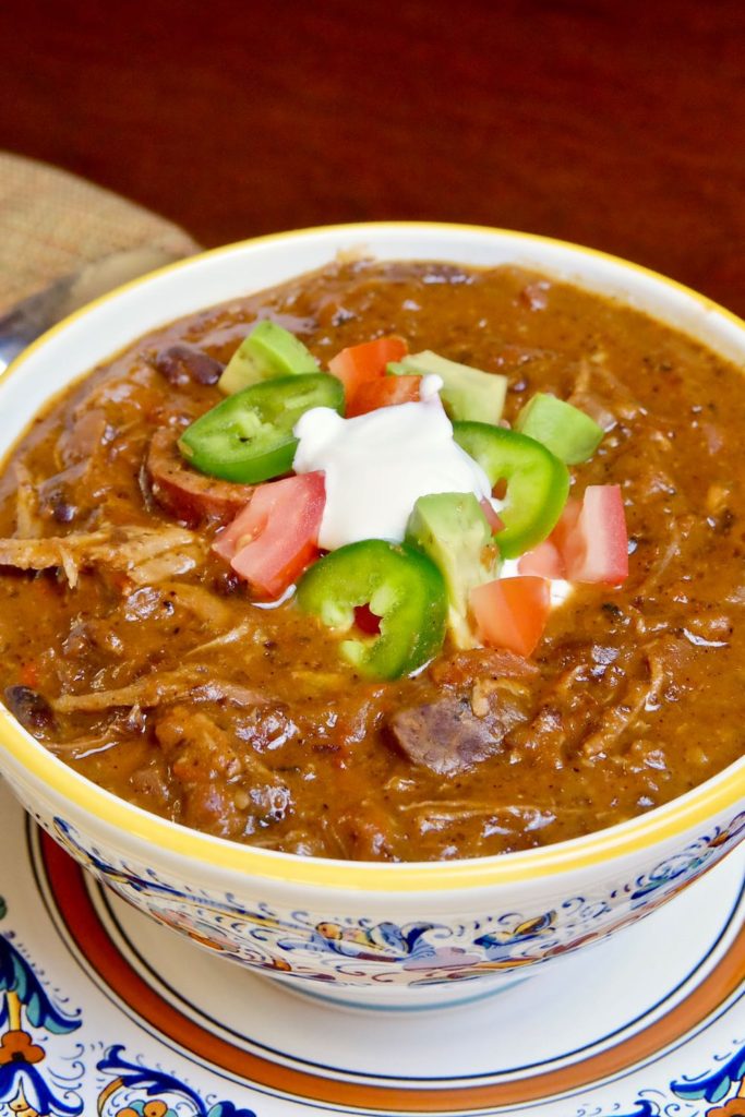 Brazilian Beef Stew Feijoada in multicolored bowl garnished with sour cream, jalapeno and chopped tomato