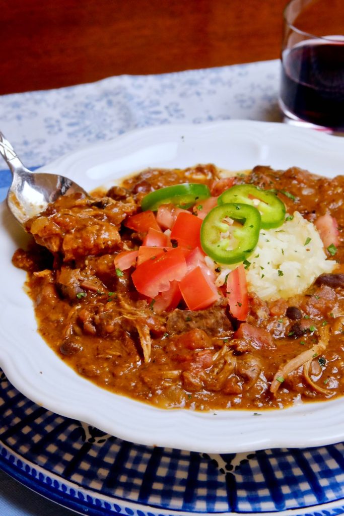 Feijoada served in white bowl set on blue and white gingham charger with a spoon shot of stew.