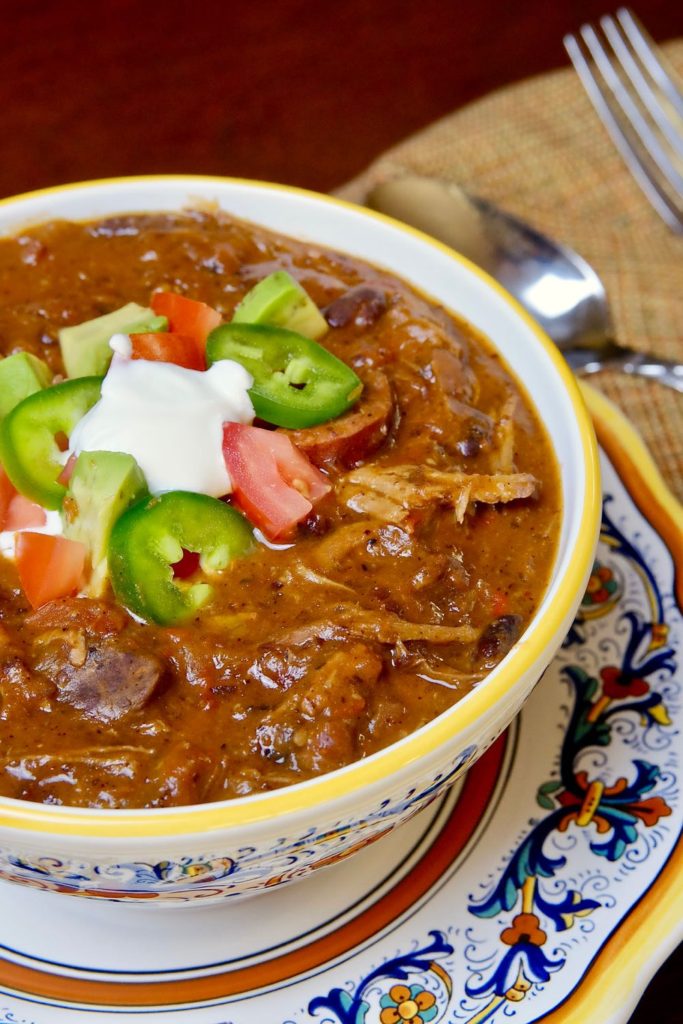 Brazilian Beef Stew Feijoada in multi-colored bowl set on matching plate with spoon in background on walnut table