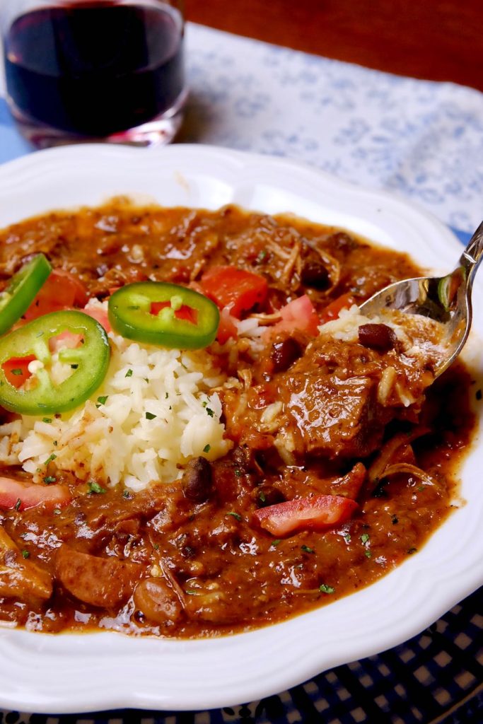 Brazilian Beef Stew in white bowl with spoon shot of meat and beans set on a blue linen placemat with wine glass in background.