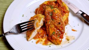 Chicken Cacciatore with bite shot served over bed of polenta on white plate.