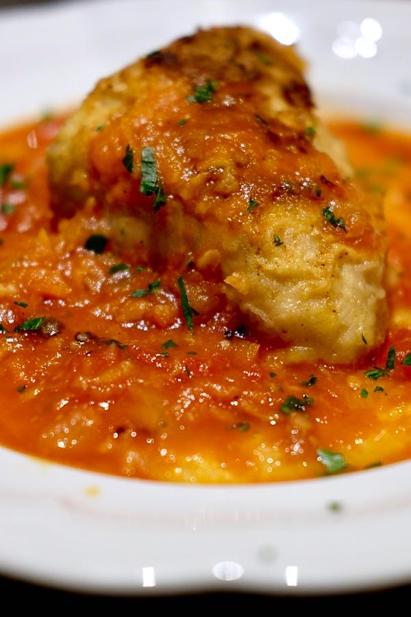 Chicken  with red sauce served over polenta in white pasta bowl