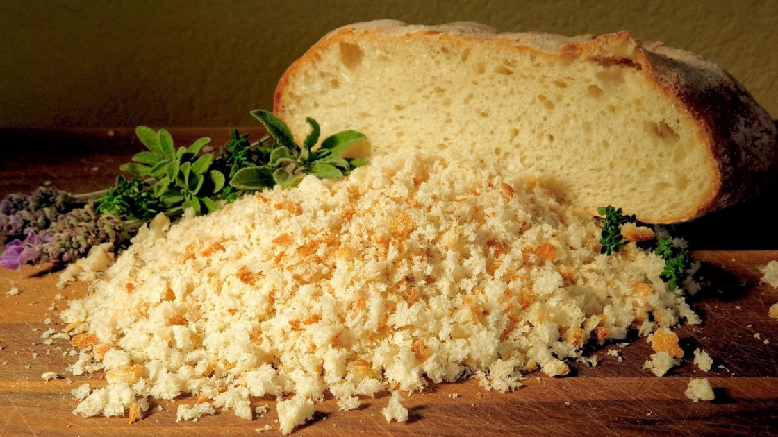Fresh Breadcrumbs with bread loaf in background with fresh herbs