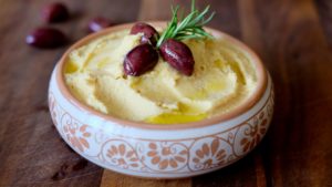 Hummus in decorative clay bowl garnished with Kalamata olives and olive oil
