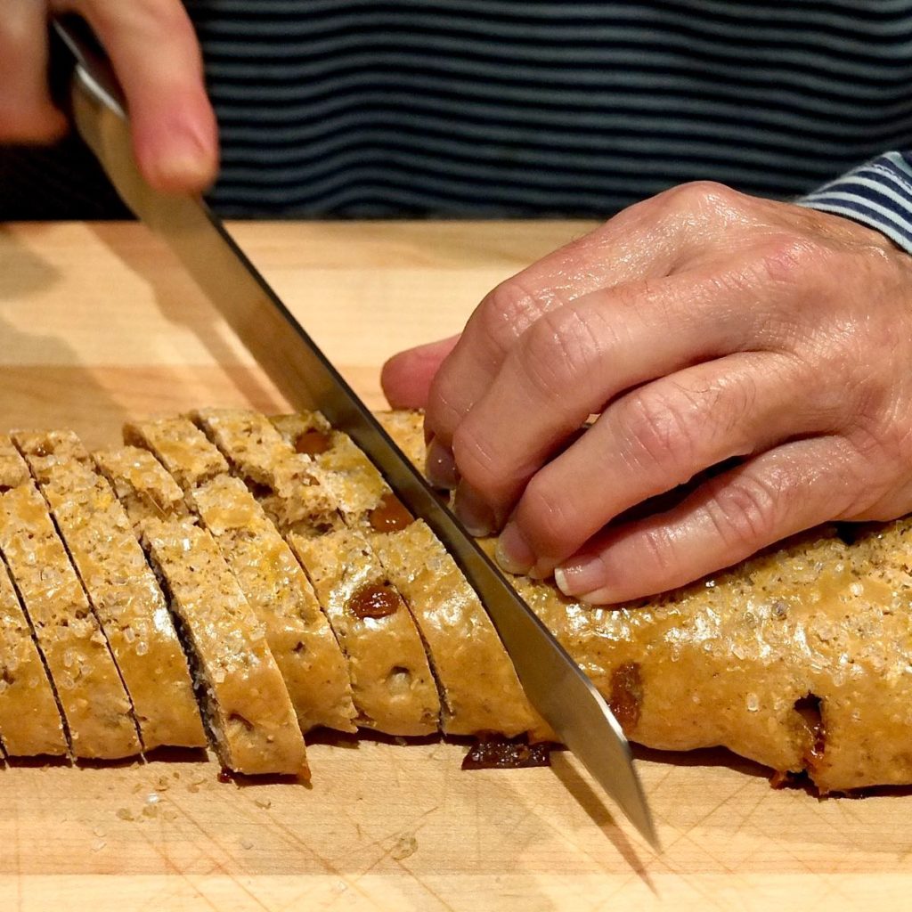  Biscotti log being cut on a maple board with serrated knife.