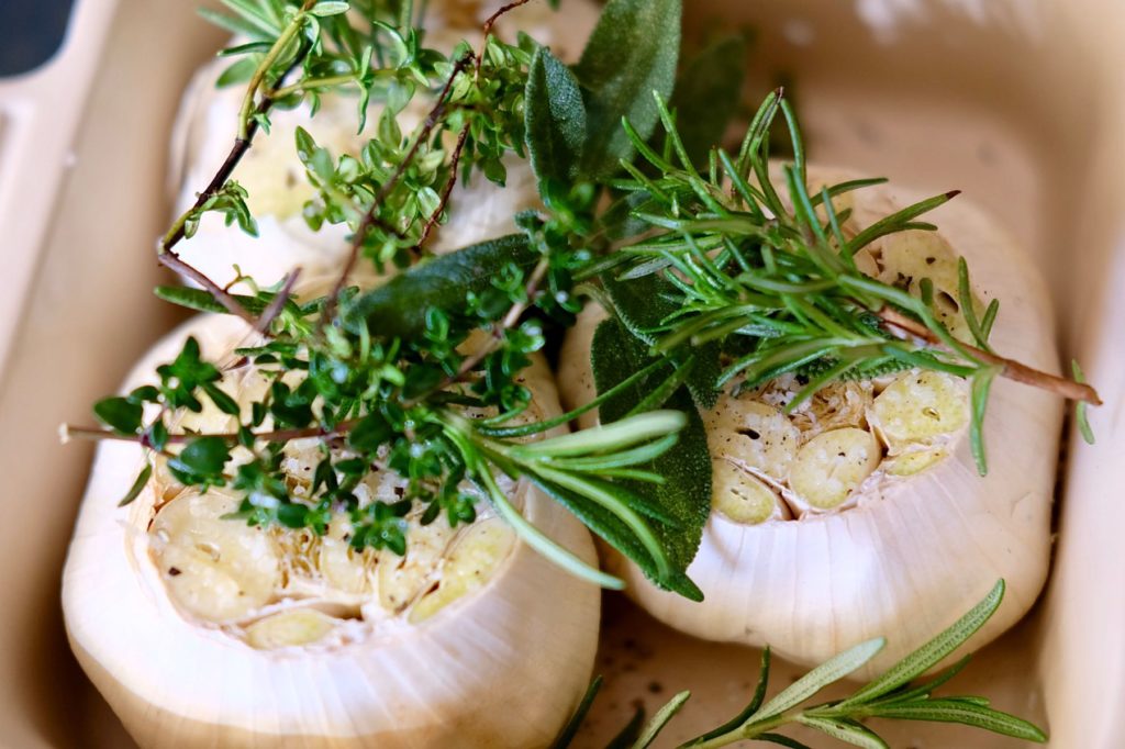Roasted Garlic in roasting dish with garnishing of herbs, before being baked