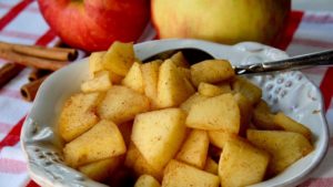 Sauteed Cinnamon Apples in serving bowl with Fresh Apples and Cinnamon stick in background.