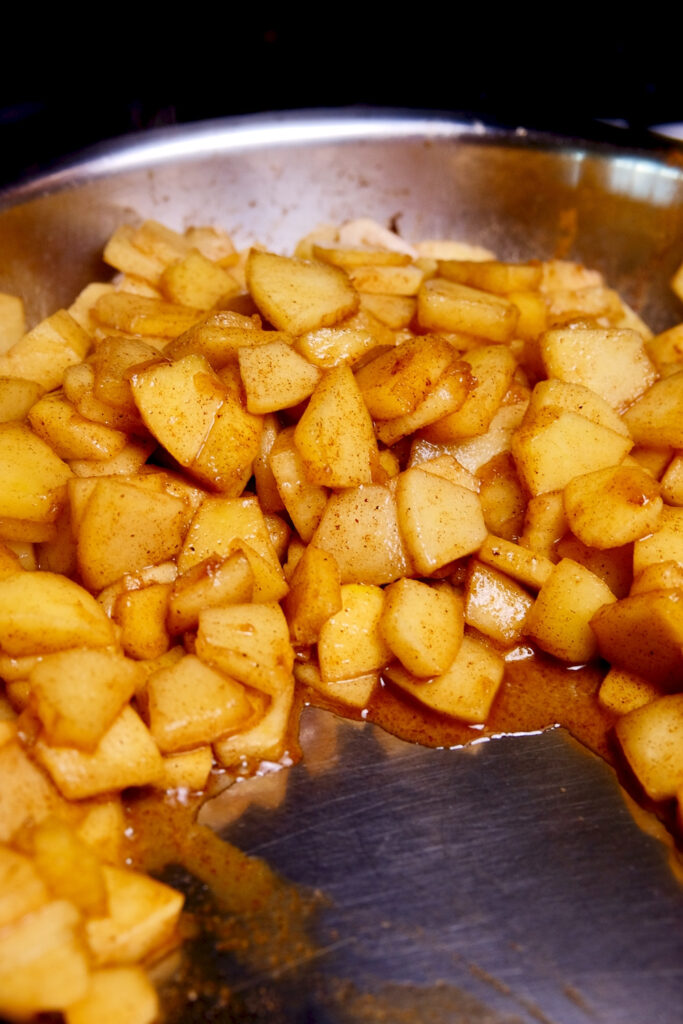 Cinnamon Apples sauteed in stainless steel pan.  Apples are pushed up to back side of pan revealing thick cinnamon syrup .