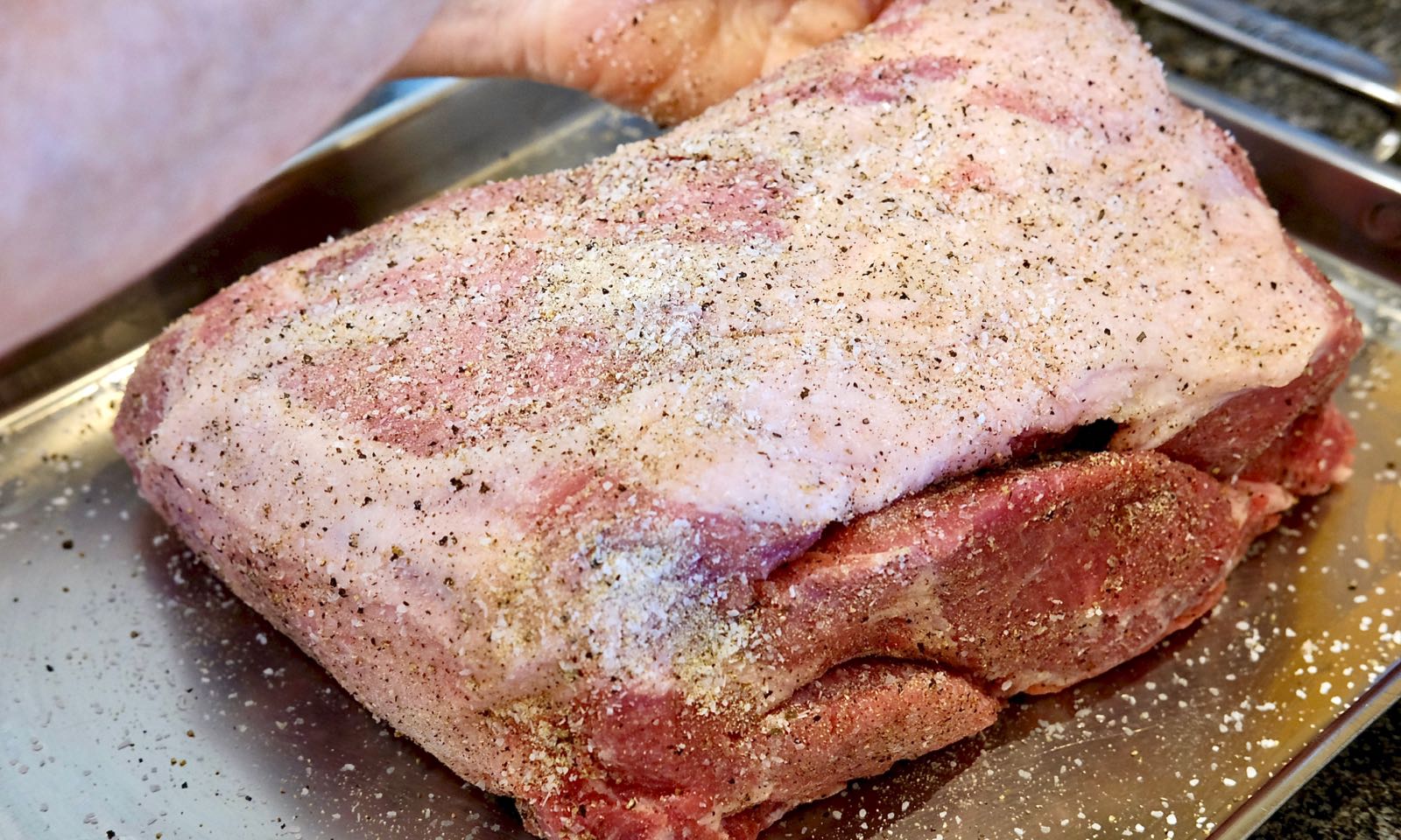 Pork Butt being seasoned on a stainless baking sheet.