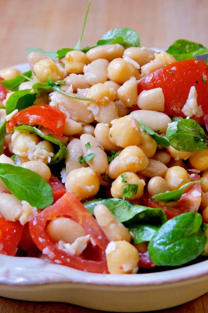 Sicilian Bean and Tomato Salad in beige serving bowl garnished with Grana Padano and arugula.