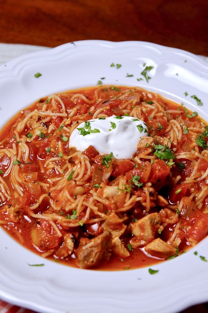 Sopa de Fideo in a white bowl garnished with a dollop of sour cream and freshly minced cilantro.