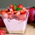 Strawberry Chiffon Cheesecake Parfait garnished with chopped fresh Straweberries and Strawberries in foreground