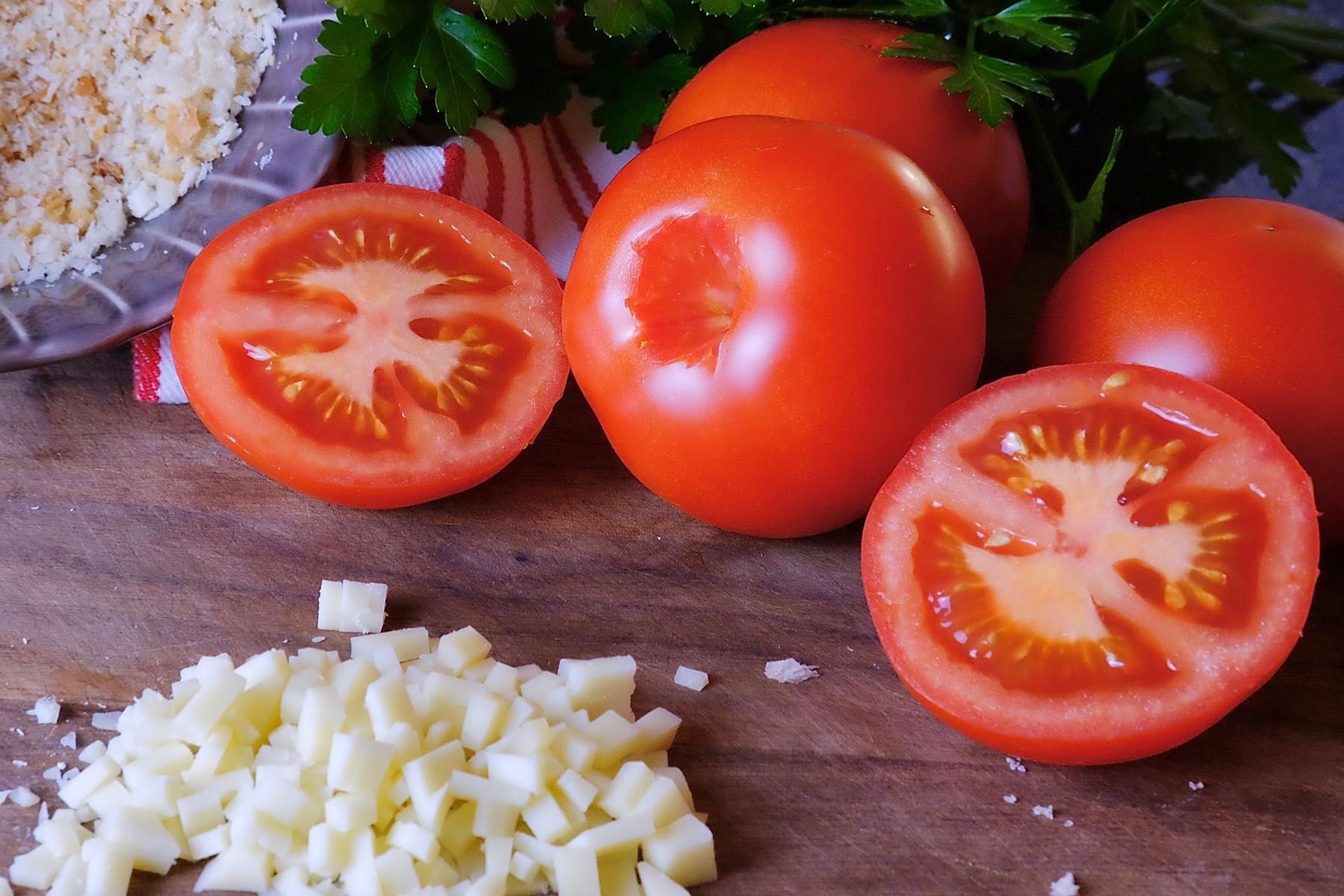 Stuffed Herb Tomatoes ingredients: diced cheese, sliced tomatoes, breadcrumbs and fresh parsley on walnut cutting board.