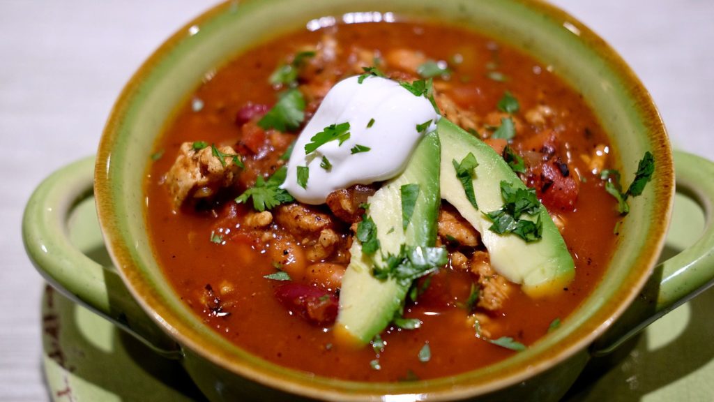 Green bowl of soup garnished with sour cream and avocado. 