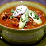 Chili Soup in green bowl, garnished with sour cream, avocado and cilantro