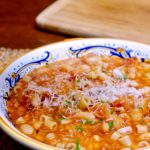 Pasta e Fagioli in gold and blue Italian bowl garnished with Parmesan cheese. Maple board in background.