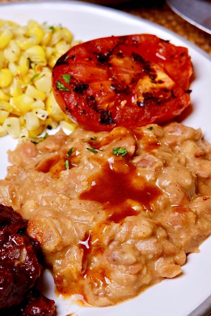 Skinny refried beans on a white plate with grilled tomato and corn.