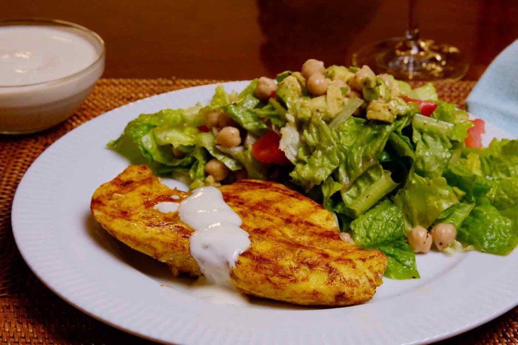 Chicken Shawarma  on a white plate with Mediterranean Salad. Wine glass is in the background of plate.