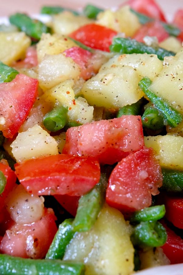Close up shot of cubed potatoes, tomatoes and green bean pieces dressed in an Italian vinaigrette. 