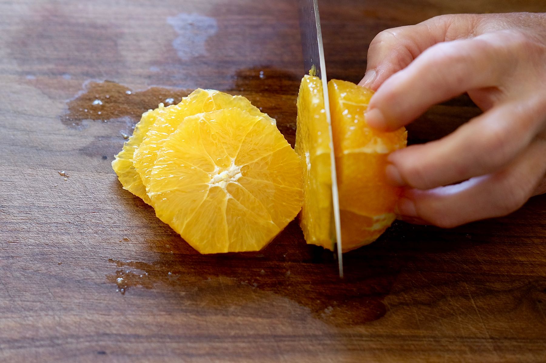 Slicing trimmed orange on cutting board.