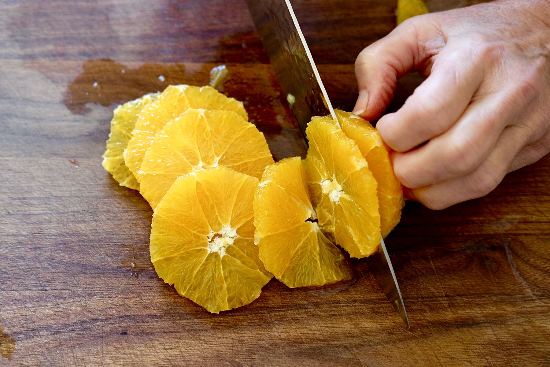 Slicing trimmed orange on cutting board.