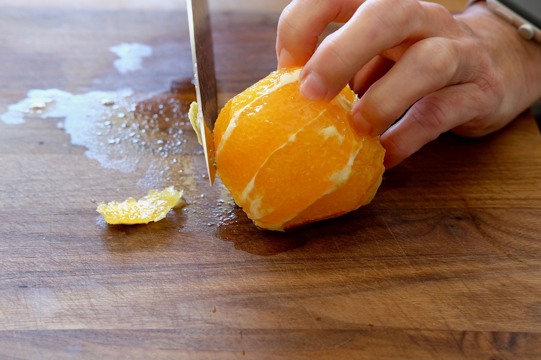 Trimming rind and pith away from orange on cutting board.