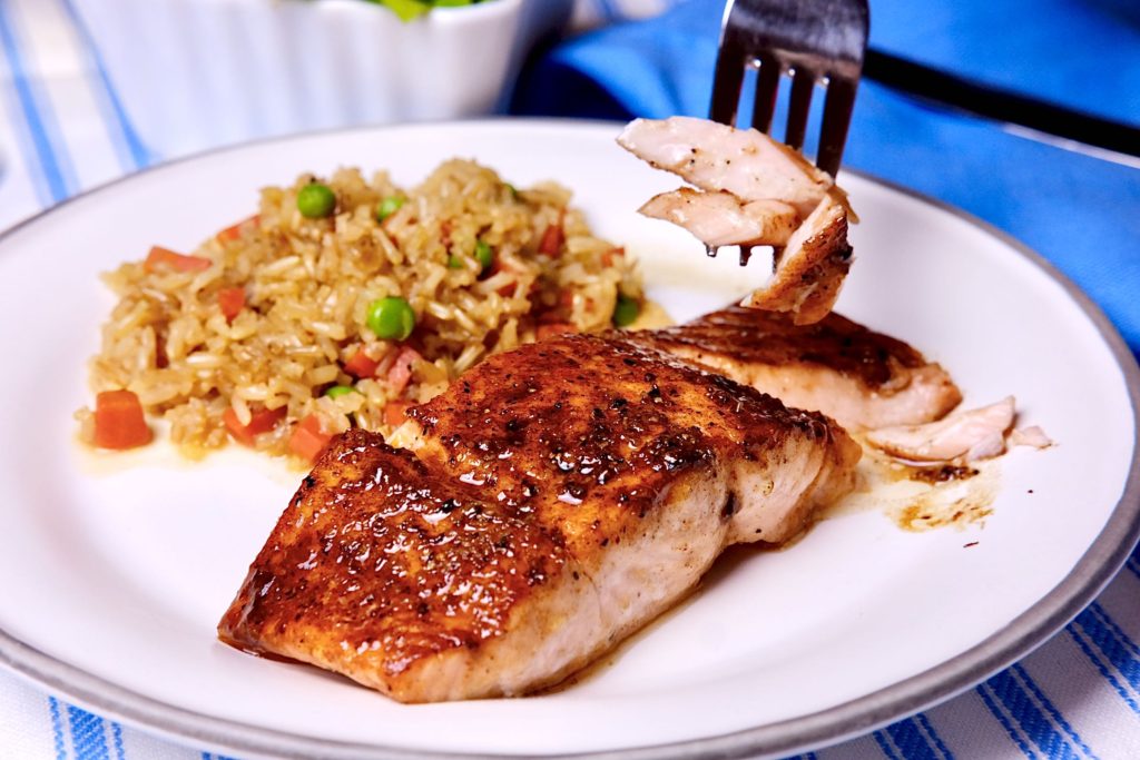 Barbecue Salmon with rice pilaf on white plate set on blue and white linens.