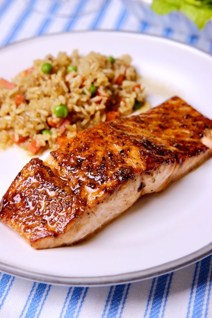 Pan Seared Barbecue Salmon on white plate with brown rice pilaf set on blue and white linen.  