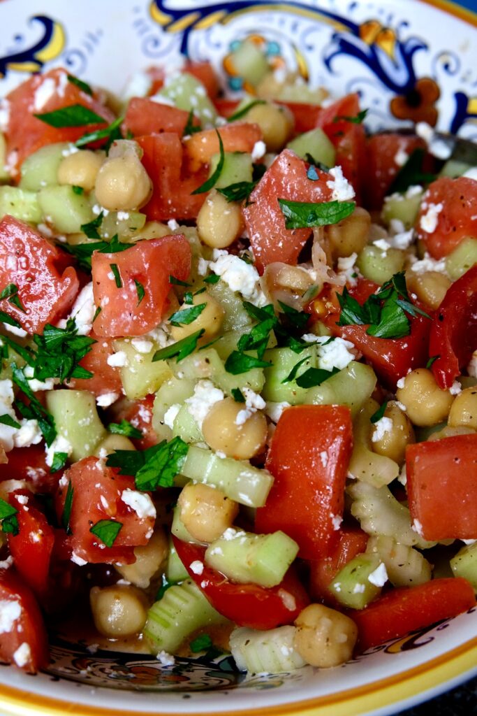 Tomato Cucumber Salad with chickpeas served in a blue and white Italian bowl garnished with crumbled Feta cheese and chopped fresh parsley.