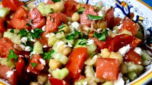 Tomato Cucumber Salad with Chickpeas in a blue and gold Italian serving bowl is garnished with crumbled Feta cheese and chopped fresh parsley