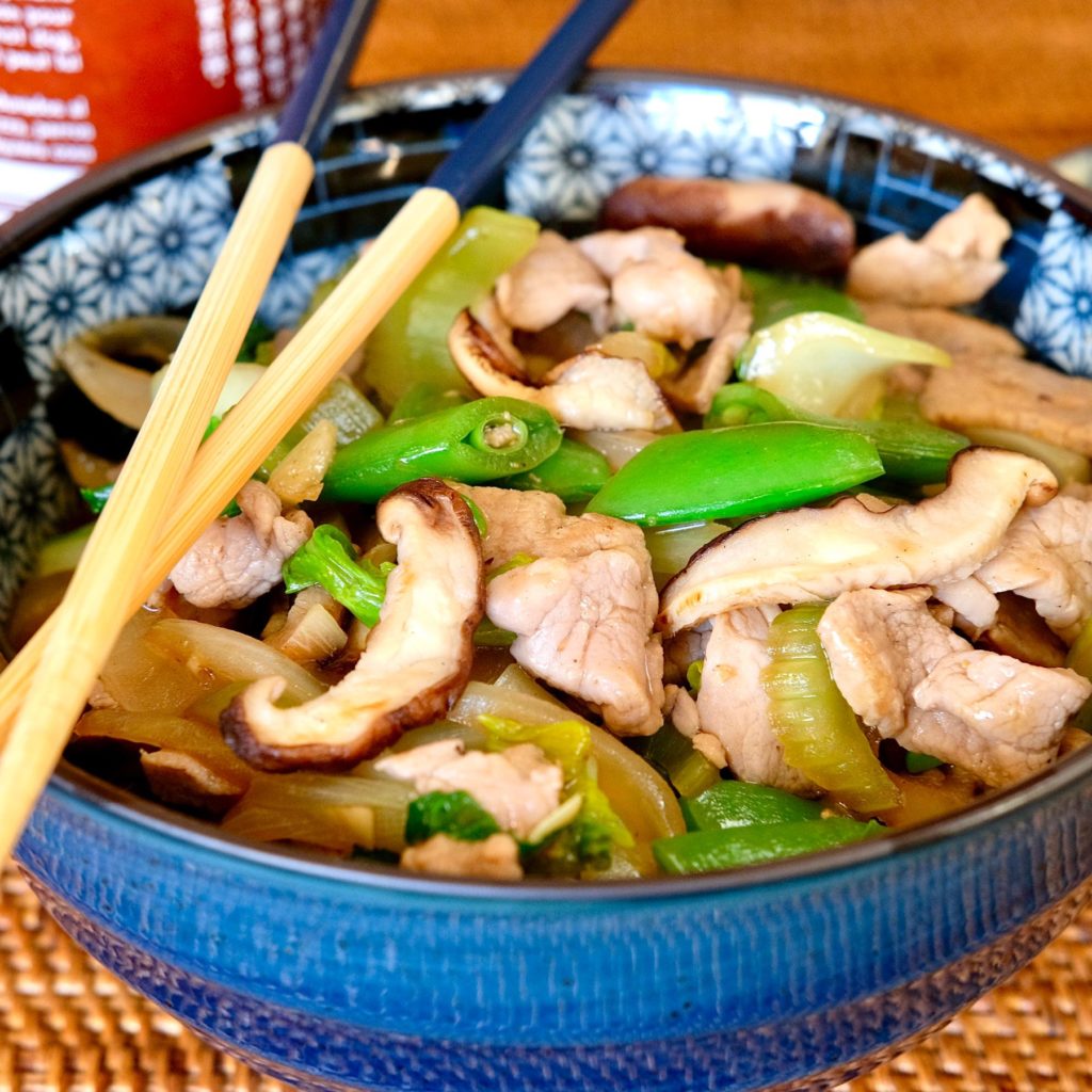 Chicken Chop Suey in blue Ramen Bowl with chopstick crossed over bowl edge and hot sauce bottle in background