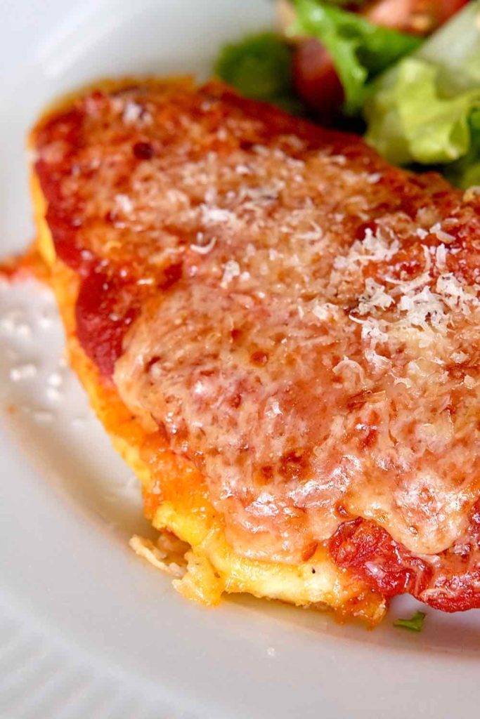 Chicken Parmesan served on a white plate with mixed green salad .