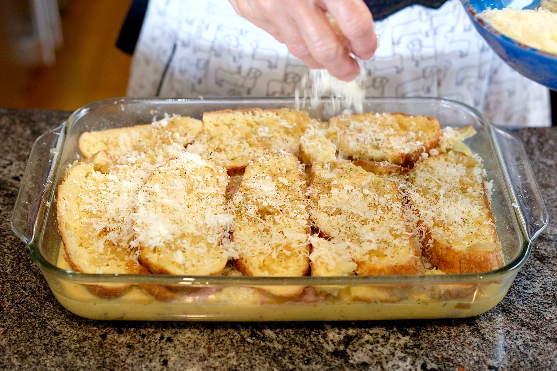 Cheese being sprinkled over top of casserole before baking. 