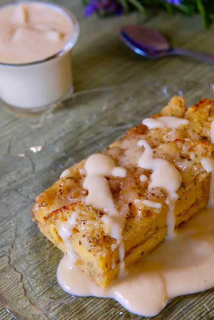 Ham and Gruyere Baked French Toast on a clear glass plate drizzled with Creamy Dijon Sauce. Glass cup with creamy dijon sauce in background.