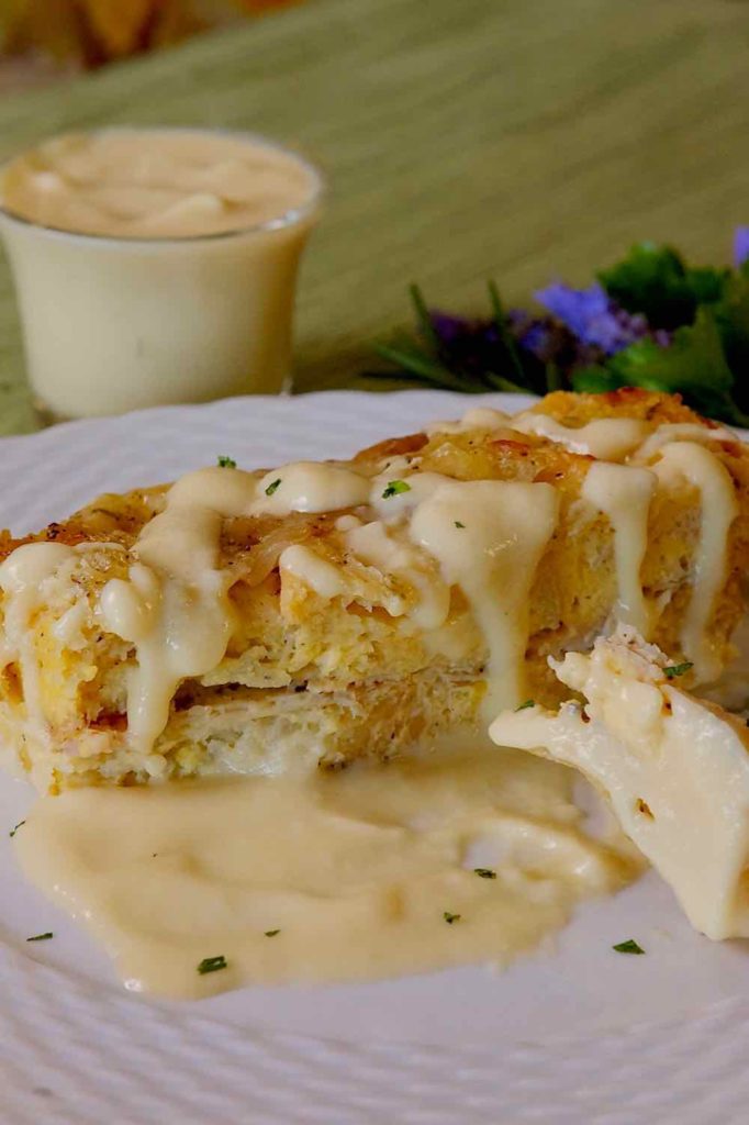 Ham and Gruyere French Toast served with Creamy Dijon Sauce on a white plate with glass vessel of sauce and bouquet of lavender flowers in background 