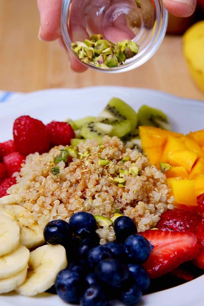 Quinoa breakfast bowl with cinnamon-orange sauce and pistachios being sprinkled over top for garnish.