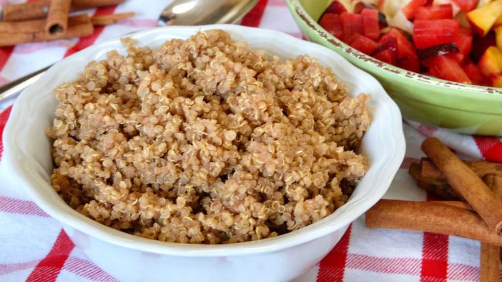 Cinnamon Almond Quinoa in white bowl with serving spoon and green bowl of chopped nectarines and plums