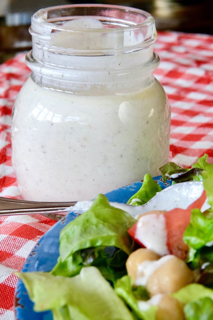 Creamy Greek Dressing in jar with salad on blue plate in foreground
