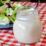 Creamy Greek Dressing in Jar on red & white checkered overlay with salad in background