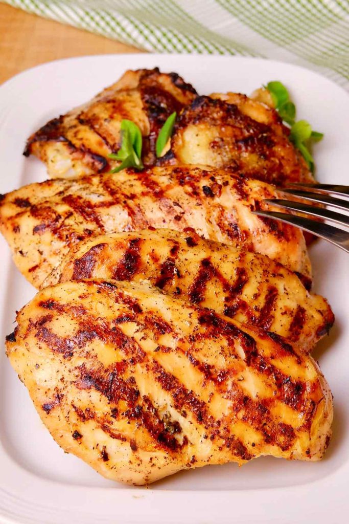 Grilled Mediterranean Chicken on white plate with serving fork and green checked linen in background.