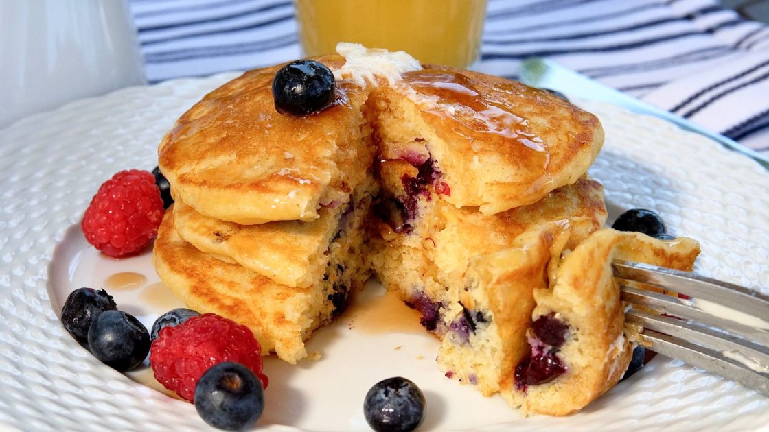 Blueberry Corn Cakes on white plate with navy striped overlay and glass of orange juice in background