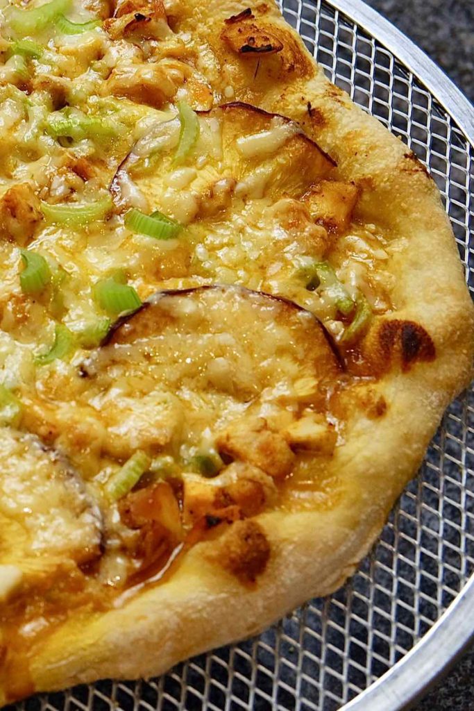 Buffalo Peach Pizza setting on a cooling rack is topped with buffalo chicken, grilled peaches, celery and gouda cheese.  