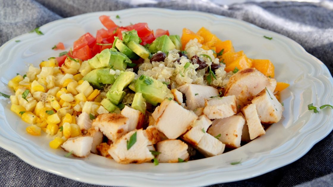 Quinoa and Black Bean Salad with vegetables, fruit and chopped chicken in white bowl