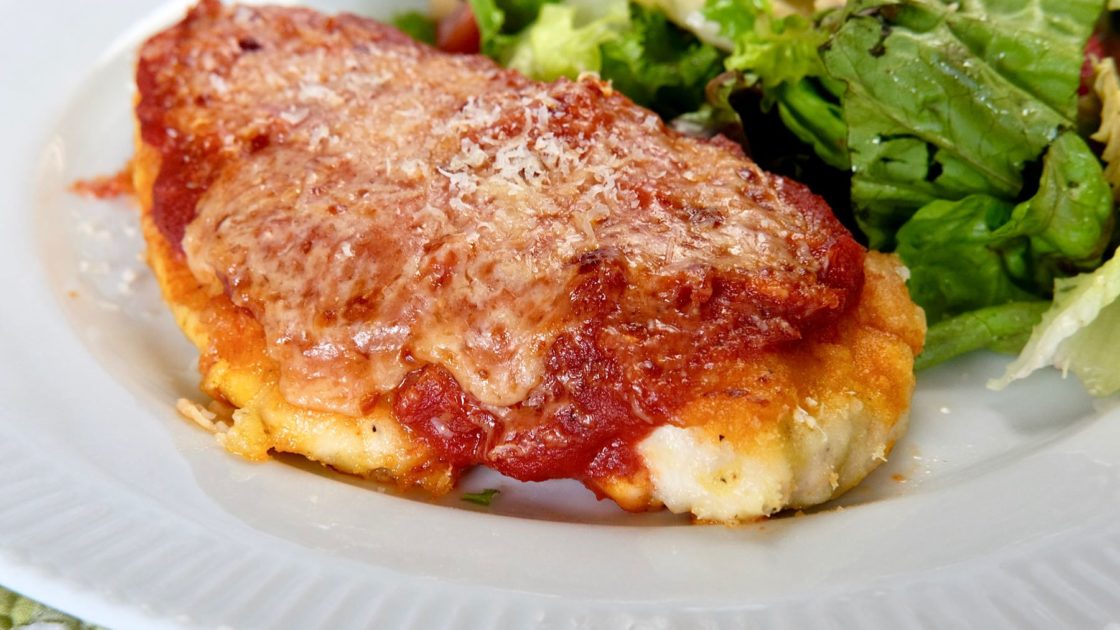 Chicken Parmesan on white plate with Mixed Green Salad