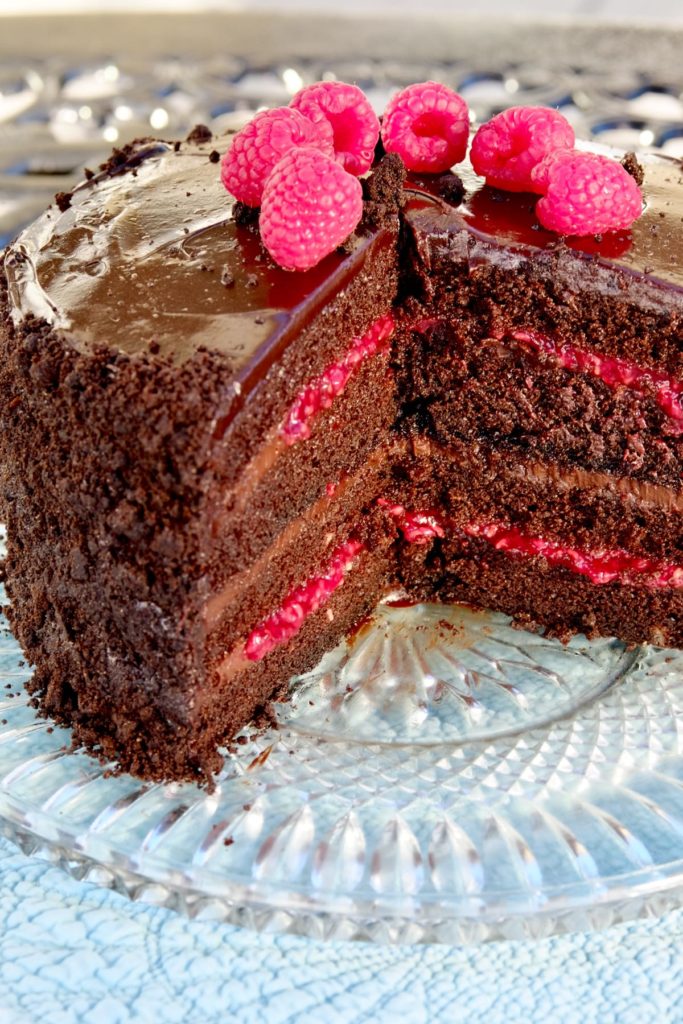 Chocolate raspberry cake garnished with Chocolate Sand on clear glass plate.